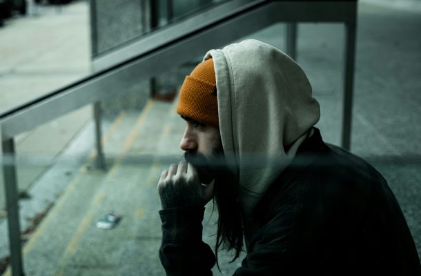 Mann in grauem Hoodie sitzt nachdenklich auf Treppe im Freien