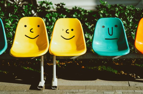 Bunte Schalenstühle mit aufgemalten Gesichtern vor Hecke im Außenbereich